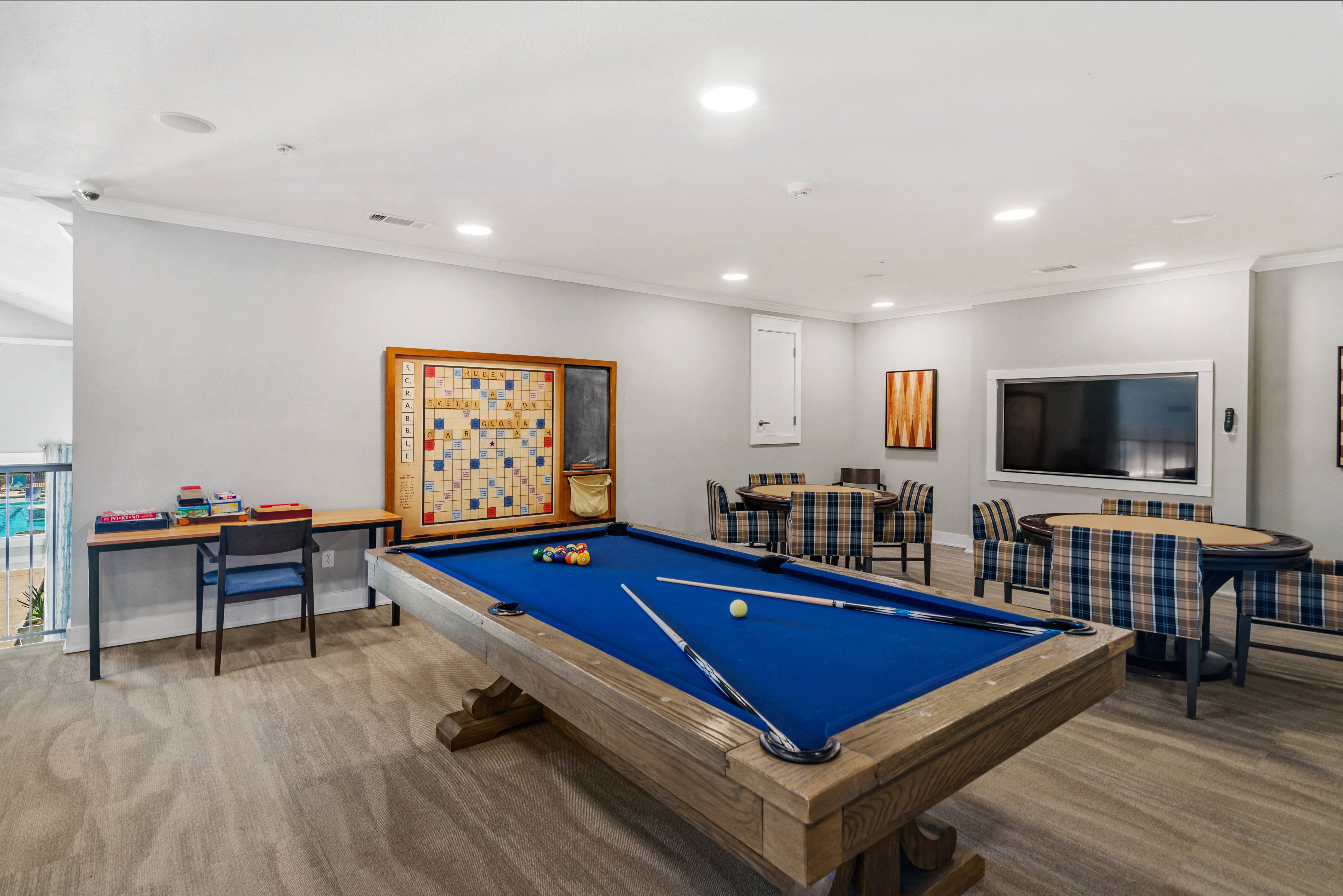 a game room with a pool table, card tables and chairs, and a television at a senior apartment community